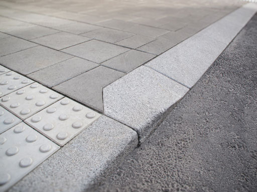 Portstens i natursten;kompletterad med taktila betongplattor med orienteringsmönster samt släta betongplattor i gångyta – i övergång mellan gångbana och körbana.