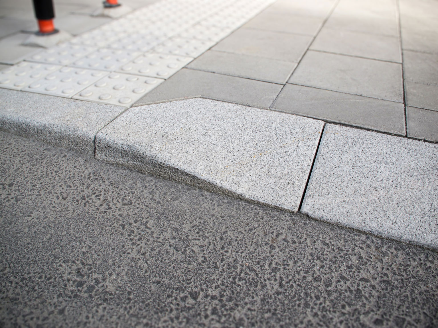 Portstens i natursten;kompletterad med taktila betongplattor med orienteringsmönster samt släta betongplattor i gångyta – i övergång mellan gångbana och körbana.