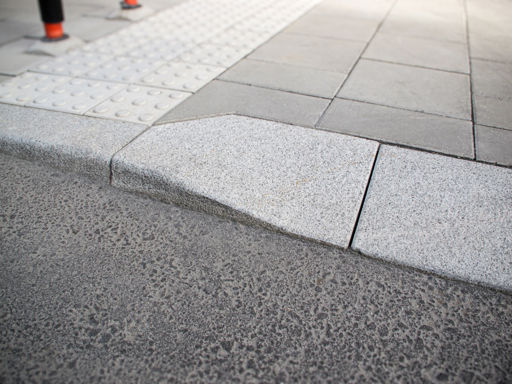 Portstens i natursten;kompletterad med taktila betongplattor med orienteringsmönster samt släta betongplattor i gångyta – i övergång mellan gångbana och körbana.