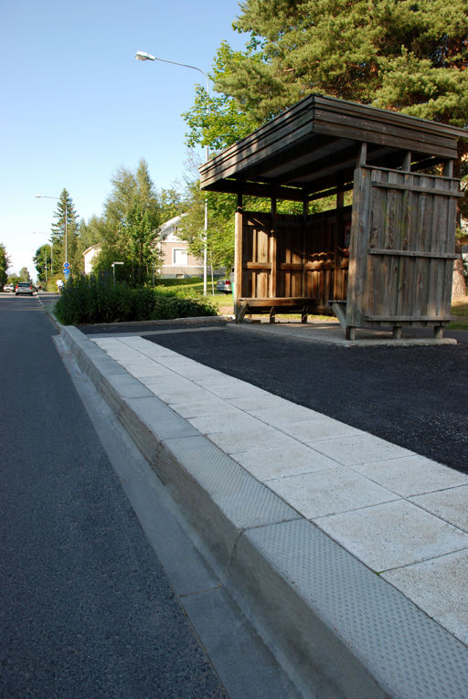 Busshållplatskantstöd monterade vid busshållplats med ett stråk av vita sinusplattor.