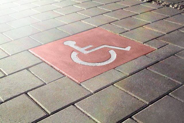 Röd symbolplatta med rullstolsmotiv i stadsmiljö